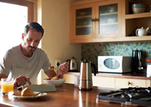 Image of a man eating fresh fruit for breakfast, while accessing the internet with mobile device.